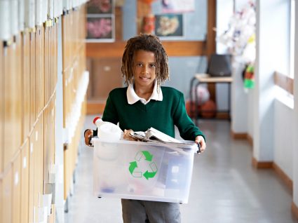 criança na escola a levar caixote com lixo para reciclar