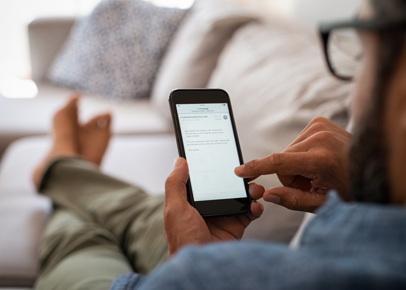 homem deitado no sofá a ver emails no telefone