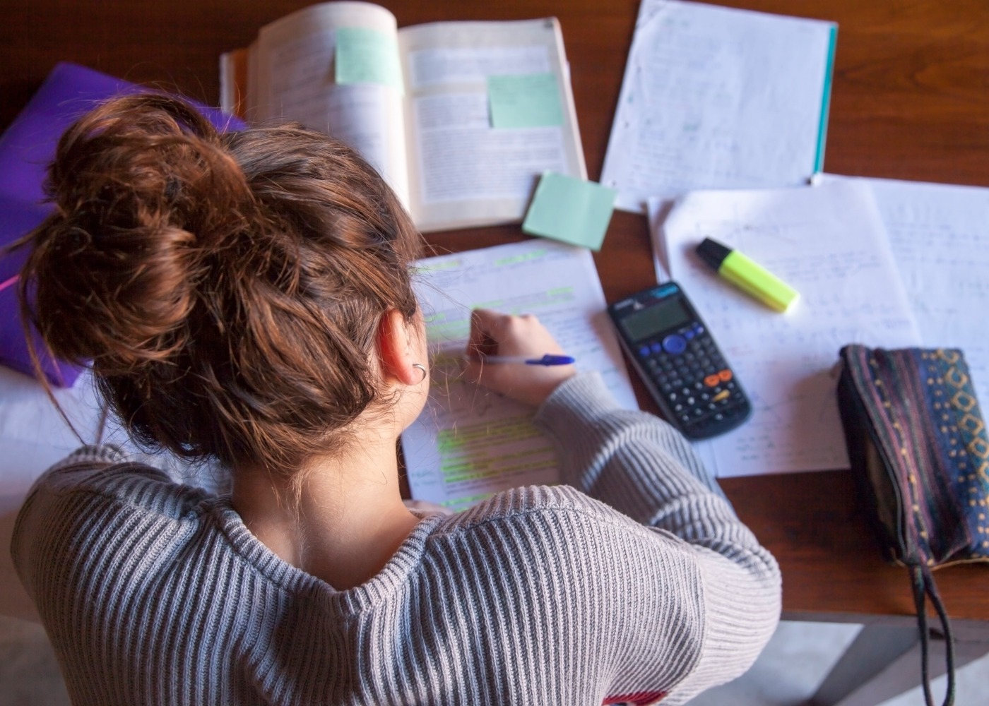 vista de cima de uma jovem a estudar com livros, calculadora e outros materiais vários