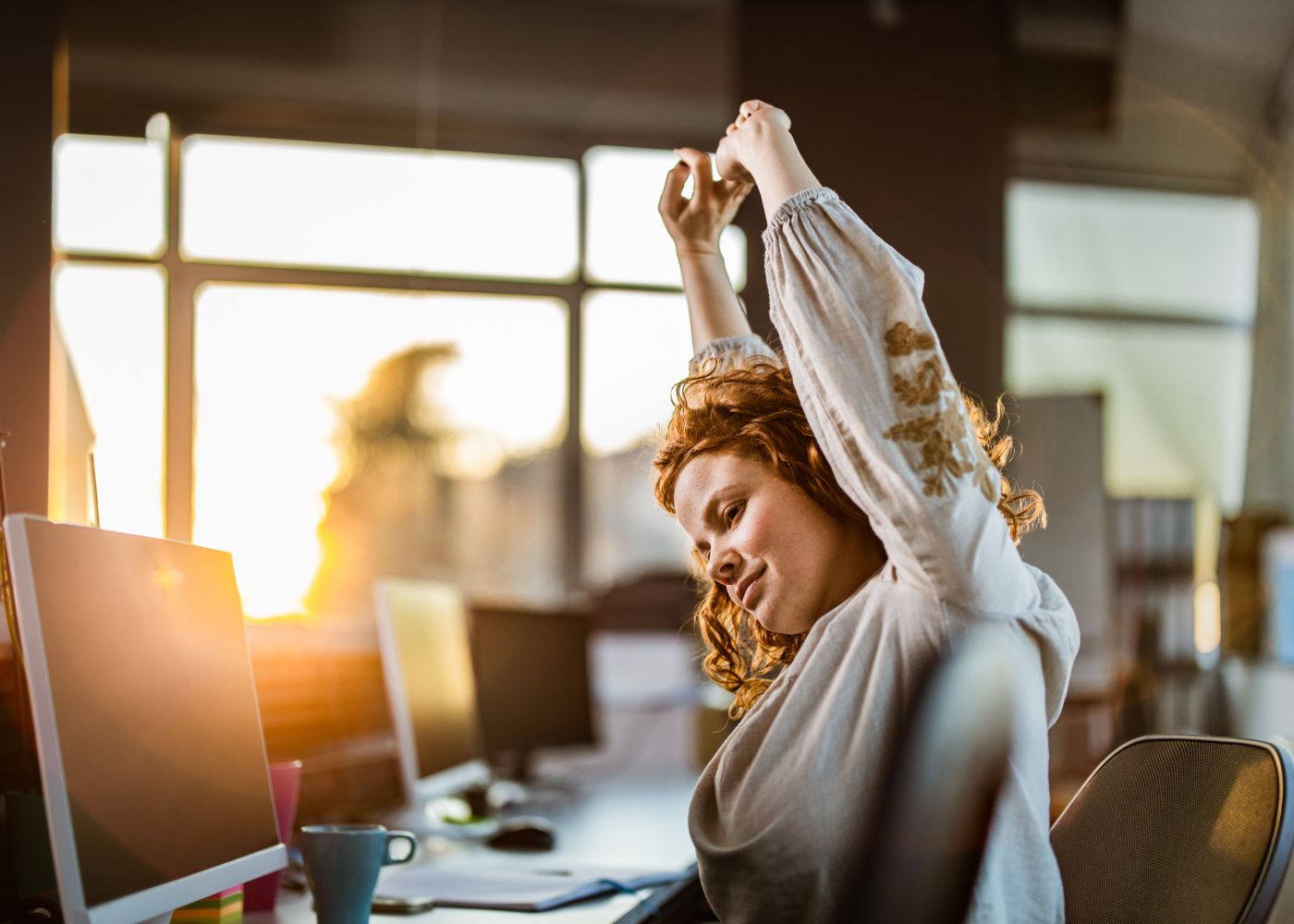 mulher em frente ao computador a fazer alongamentos como um dos exercícios para fazer no escritório