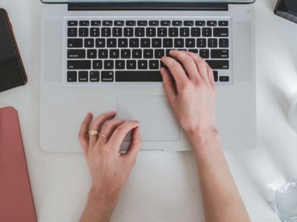 mãos de mulher ao computador com telefone e agenda ao lado