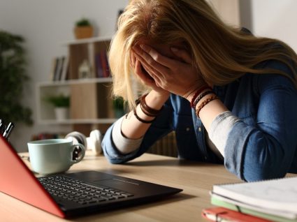 mulher ao computador com mãos na cabeça por exercer uma das profissões que causam mais stress