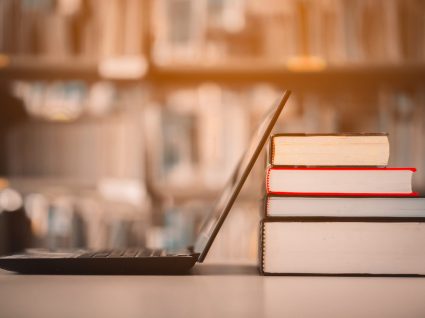 livros e computador aberto em cima de mesa de biblioteca