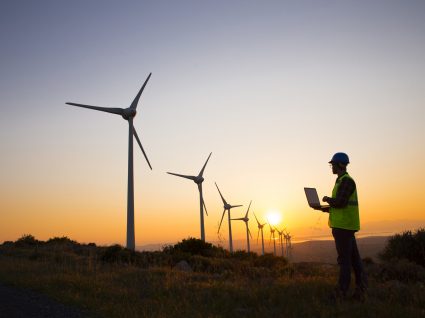 homem ao por do sol a analisar ventoinhas de energia eólica