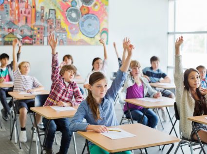 alunos na sala de aula com a mão no ar para participar