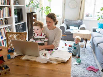 mãe a fazer teletrabalho com um filho ao colo e outro a brincar no chão