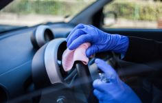 pessoa a passar pano no volante e limpar os plásticos do carro
