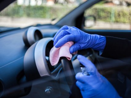 pessoa a passar pano no volante e limpar os plásticos do carro