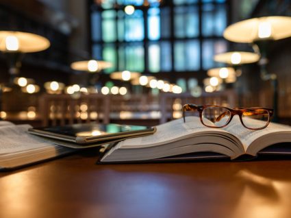 livros e óculos pousados em cima de uma mesa na biblioteca