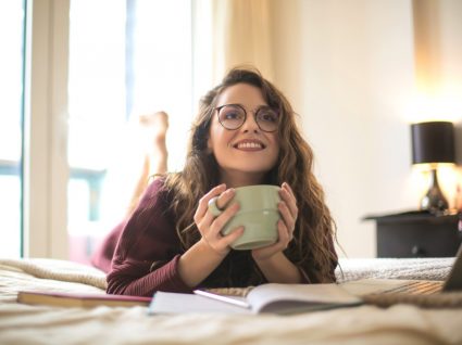 jovem mulher pensa em como fazer dinheiro em investir enquanto bebe um café deitada na cama