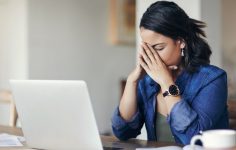 mulher ao computador com mãos na cara de cansaço