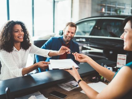 casal a analisar com funcionária de stand as melhores opções para comprar carro