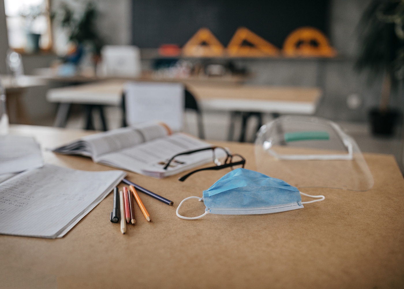 mesa de escola com máscara, viseira e materiais escolares