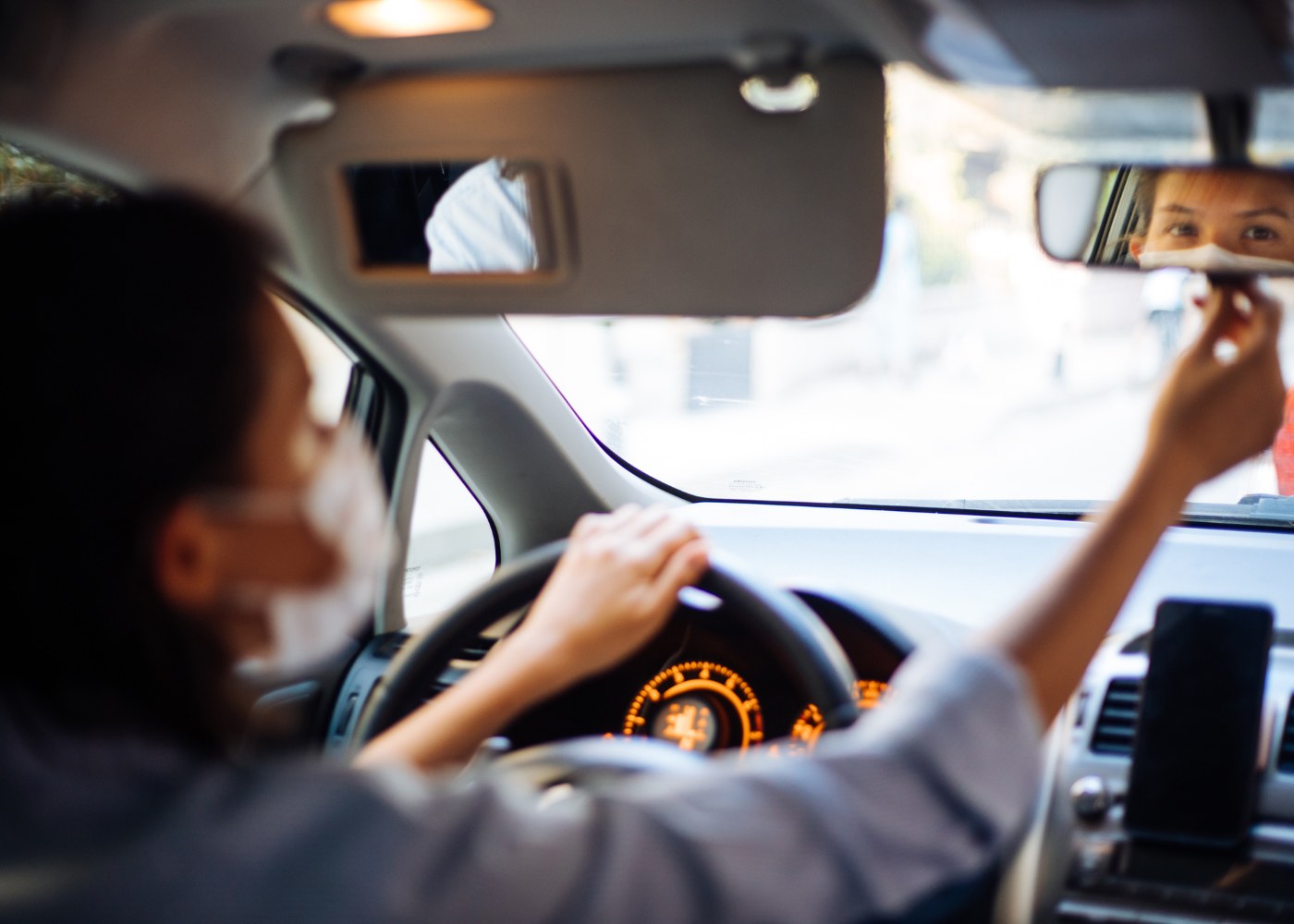 mulher com máscara a ajustar o espelho retrovisor do carro